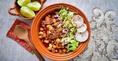 an orange bowl filled with food next to a wooden spoon and two lime wedges