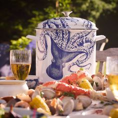 a blue and white pot sitting on top of a table filled with food next to wine glasses