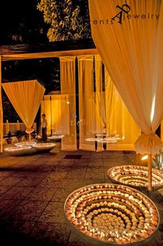 an outdoor area with candles lit up on the ground and white drapes covering it