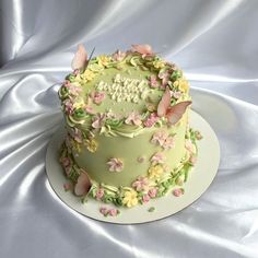 a birthday cake decorated with flowers and butterflies on a white tableclothed surface,