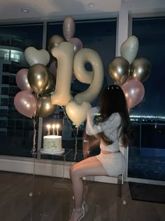 a woman sitting on a chair in front of balloons with the number 19 spelled out