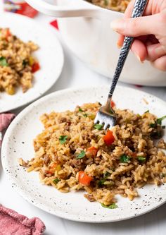 someone is holding a fork over some rice on a white plate with other dishes in the background