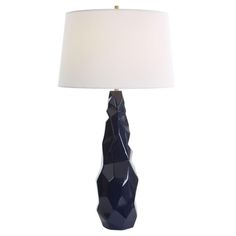 a table lamp with a white shade on the base and a dark blue vase shaped like a face