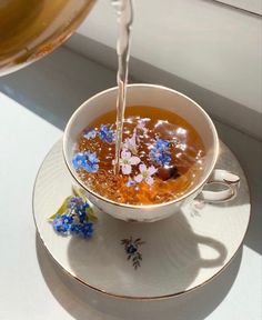 a tea cup filled with liquid being poured into it on top of a saucer