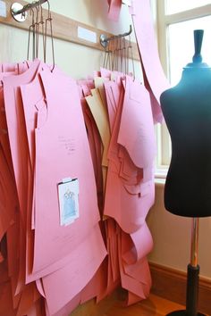 there are many pieces of pink paper hanging on the clothes rack next to a mannequin