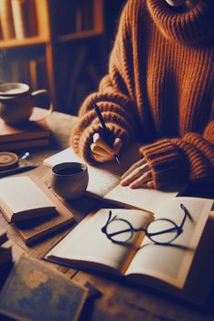 a person sitting at a table with books and glasses on it, writing in a notebook