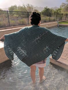 a woman is standing in the water wearing a green crocheted shawl over her shoulders