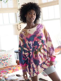 a woman standing in front of a window wearing a colorful sweater