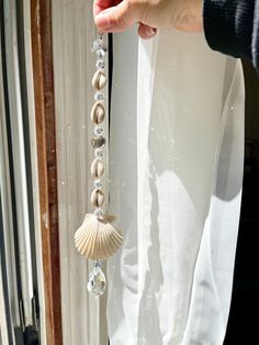 a person is holding a beaded necklace with seashells hanging from it's side