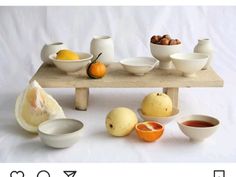 a table topped with white bowls filled with fruit next to oranges and pears