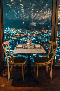 two chairs sit at a table in front of a large window overlooking the city lights