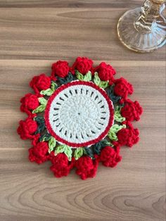 a crocheted doily with red flowers and green leaves on a wooden table