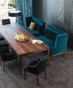 a wooden table with blue chairs and a plate of fruit on it in front of a window