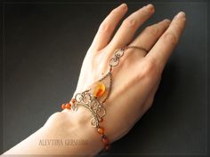 a woman's hand wearing a bracelet with orange beads and an ornate cross on it