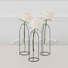 three vases with white roses in them on a table top, one is empty