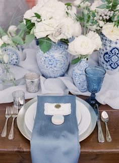 the table is set with blue and white dishes, silverware, and flowers in vases