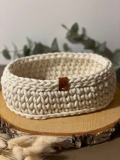 a white crochet basket sitting on top of a wooden table next to a plant