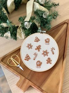 a wooden tray holding a cross - stitch hoop and scissors next to a christmas wreath