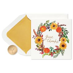 a card with an orange and yellow floral wreath on it, next to a gold envelope