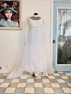 a white dress is on display in front of a blue door with a painting behind it