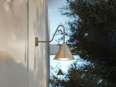 an outdoor wall light on the side of a white building with trees in the background