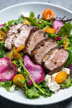 a white plate topped with meat and veggies on top of a marble table