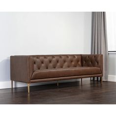 a brown leather couch sitting on top of a hard wood floor next to a window