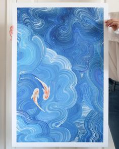 a woman holding up a blue and white painting with two koi fish in it