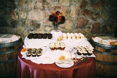 a table topped with cupcakes and desserts next to two wine casks