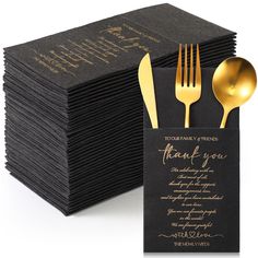 a stack of black napkins with gold forks and spoons on top of it