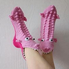 a pair of pink crocheted slippers with eyes and claws on the feet