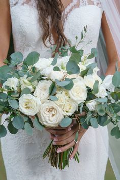 a bride holding a bouquet of white roses and greenery