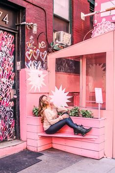 a woman sitting on a bench in front of a pink building with graffiti all over it