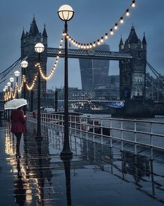 a woman with an umbrella is walking down the street in the rain by tower bridge