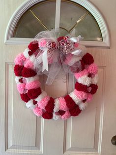 a pink and red wreath hanging on the front door to a white door with a bow