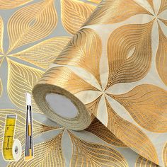 a roll of tape next to a wallpaper with gold leaves on it and a ruler