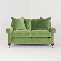 a green couch with two pillows on the arm and one pillow on the back, sitting in front of a white wall