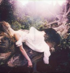 a woman laying on top of a tree trunk in the middle of a forest with her eyes closed