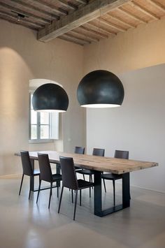 a dining room table surrounded by black chairs and two large lamps hanging from the ceiling