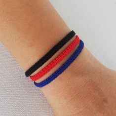 three bracelets with red, white and blue thread on the wrist are shown in close up