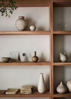 the shelves are filled with vases, bowls and other decorative items in white and wood