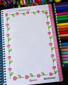 an open notebook with pink flowers on it and colored crayons in the background