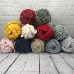 a pile of multicolored towels sitting on top of a white wooden floor next to a brick wall