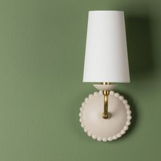 a white lamp on a green wall next to a light fixture with a white shade