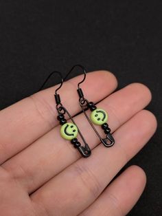 pair of black and green earrings with smiley face on each earring, in the shape of two dangling hooks