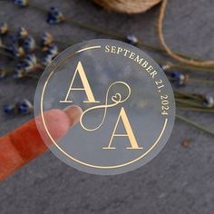 a person holding up a round sticker with the letter a on it and lavender sprigs in the background