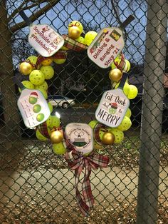 a wreath made out of tennis balls and other items hangs on a chain link fence