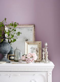 a white mantle topped with vases filled with flowers next to a mirror and framed pictures