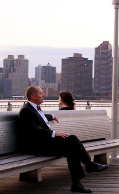 a man and woman are sitting on a bench in front of the cityscape