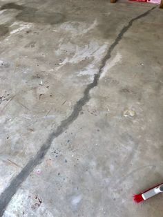 a red brush sitting on top of a cement floor next to a wooden table and chair